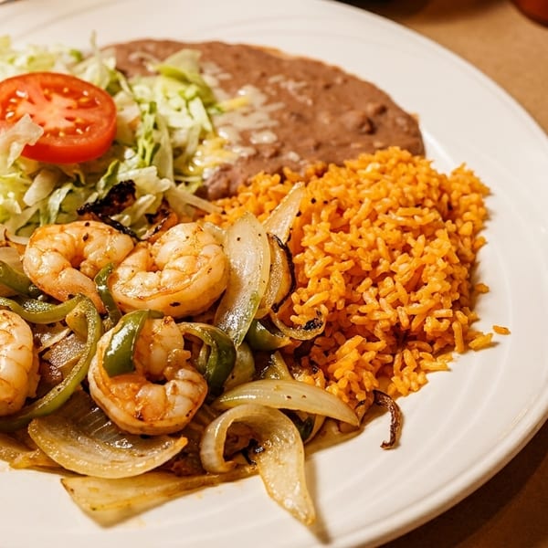 Shrimp fajitas with grilled onions and peppers, rice, refried beans, lettuce, tomato, and tortillas.
