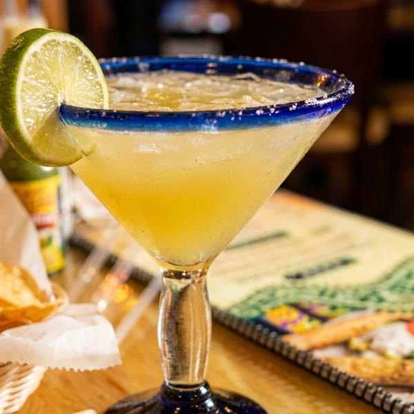 Margarita with a lime slice and salted rim, next to a basket of tortilla chips and a menu.
